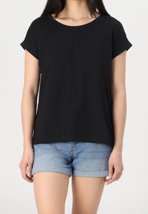 Woman wearing a black short-sleeve shirt and light blue rolled-hem denim shorts against a plain background.