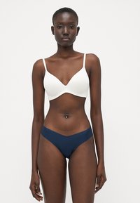 Witte zachte beha met dunne bandjes, gecombineerd met blauwe bikini-slipjes. Glad materiaal met een subtiele glans, met een lage pasvorm.