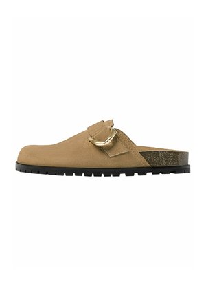 Tan suede slip-on clog with adjustable gold buckle, contoured cork footbed, and black rubber tread sole.