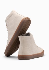 Krémové vysoké tenisky s hladkým semišovým povrchem, gumovou podrážkou s herringbone vzorem a kontrastním hnědým dnem. Disponují klasickým designem na šněrování.
