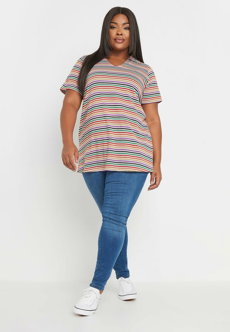 Randig kortärmad T-shirt med V-ringning i flerfärg, med horisontella ränder. Åtföljd av blå skinny jeans och vita sneakers.