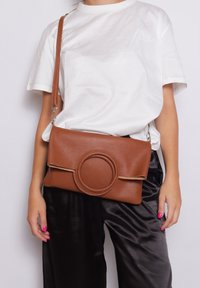Borsa a tracolla in pelle marrone con accentuazione circolare, texture liscia, forma rettangolare e tracolla removibile.