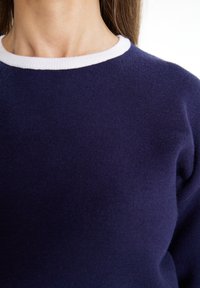 Granatowy sweter z białym ściągaczem, wykonany z miękkiej dzianiny, z prostym okrągłym dekoltem i gładką fakturą.