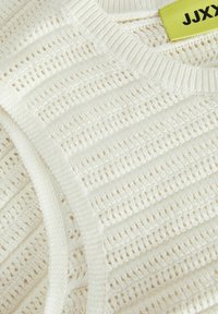 Weißer Strickpullover mit einem strukturierten, offenen Gewebemuster und horizontalen Streifen; enthält ein sichtbares Etikett mit "JJXY."