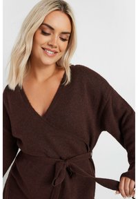 Brun inslagssweater med djup V-hals, långa ärmar och knytdetalj vid midjan. Mjuk textur med subtila färgvariationer.