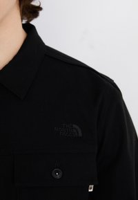 Chemise noire avec col boutonné et poche à rabat ornée d'un logo brodé noir. Confectionnée dans un tissu texturé.