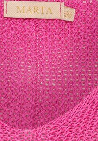 Rosa stickad tyg med lös väv och en texturerad yta. Har en beige etikett med "MARTA" i guldskrift nära toppen.