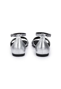 Zilveren leren sandalen met enkelbandjes, open achterkant en ronde neus. Glad metallic oppervlak en een platte zwarte zool, minimale ontwerpaccenten.