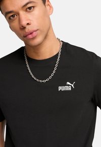 Tricou negru din bumbac cu guler rotund și mâneci scurte, având logo-ul alb "PUMA" și un grafic mic cu un puma pe pieptul stâng. Colier din lanț argintiu.