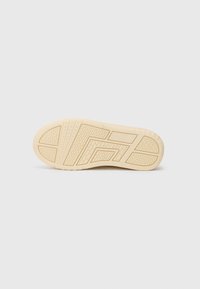 Semelle de chaussure en caoutchouc beige avec des motifs texturés, y compris des rainures surélevées, et un bord plat. Zone des orteils arrondie et surface lisse et solide.