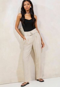 Pantalones de tiro alto en color beige con un cinturón que tiene una hebilla plateada, combinados con un bodysuit negro de canalé y sandalias minimalistas negras.