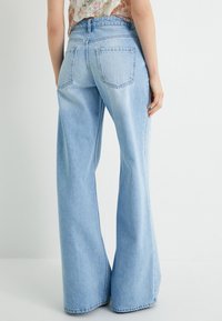Jeans de mezclilla de pierna ancha en azul claro con cintura alta, que presentan un diseño clásico de cinco bolsillos y una textura descolorida. Se muestra vista trasera.