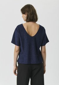 Top de culoare bleumarin, cu mâneci scurte și spate adânc în V. Fabricat dintr-un material strălucitor, având o croială lejeră și o textură moale.