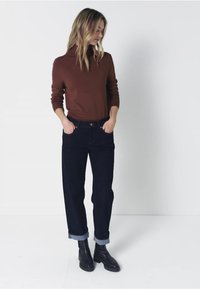 Suéter de pico marrón, jeans oscuros de tiro alto con los puños enrollados y botas negras al tobillo. Diseño sencillo con un ajuste relajado.
