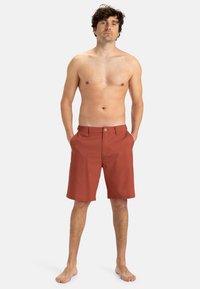 Herren-Shorts in Rostfarbe, aus leichtem Stoff, mit flachem Frontdesign, Gürtelschlaufen, zwei frontalen Taschen und einem einzelnen Knopfverschluss.