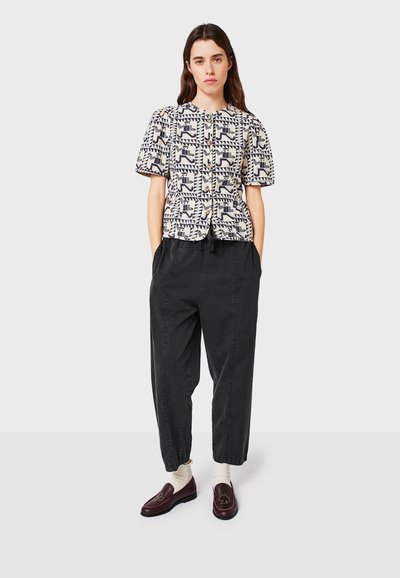 Blusa a maniche corte di colore crema con stampa geometrica blu navy, design con bottoni, abbinata a pantaloni larghi neri e mocassini bordeaux.