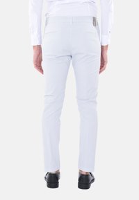 Pantaloni slim-fit grigio chiaro con una texture liscia, tasche posteriori discrete e design a gamba affusolata, abbinati a scarpe nere.
