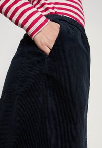 Falda de pana en color marino con ribetes verticales, que cuenta con un bolsillo lateral, combinada con una camiseta de manga larga a rayas rojas y blancas.