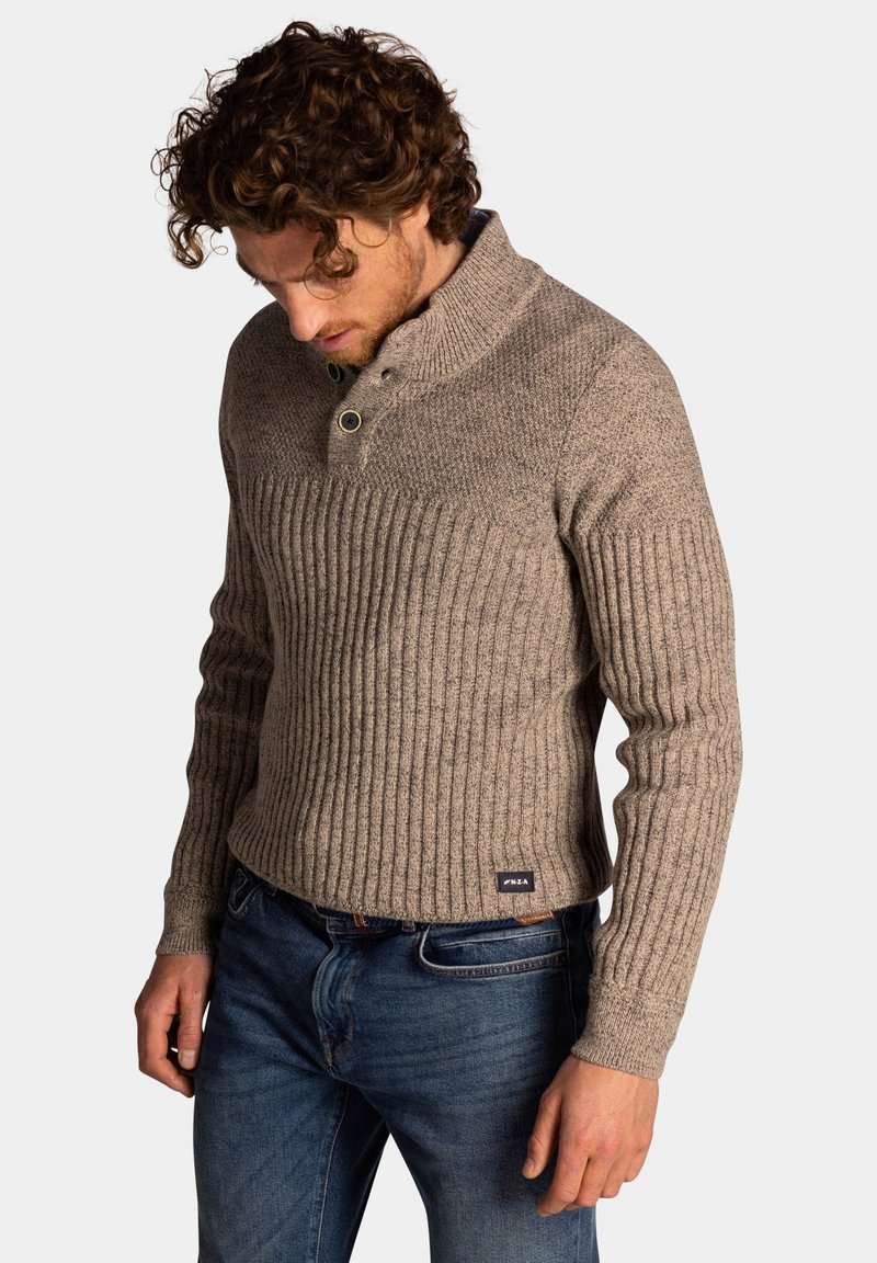 Bruine geribde gebreide trui met hoge kraag, voorzien van twee knopen en een gestructureerde stof. Gemaakt om te dragen met blauwe spijkerbroeken.