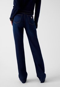 Denim jeans met wijde pijpen in donker marineblauw, met een gladde textuur, twee achterzakken en een klein logoplaatje bij de tailleband.