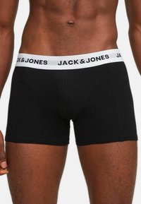 Schwarze Boxershorts aus glattem Stoff mit einem weißen Gummibund, auf dem das Logo "JACK & JONES" abgebildet ist. Enganliegendes Design und mittellange Oberschenkel.