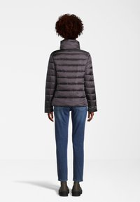 Doudoune gris foncé, avec un motif matelassé horizontal et un col haut. Associée à un jean bleu et des bottines.