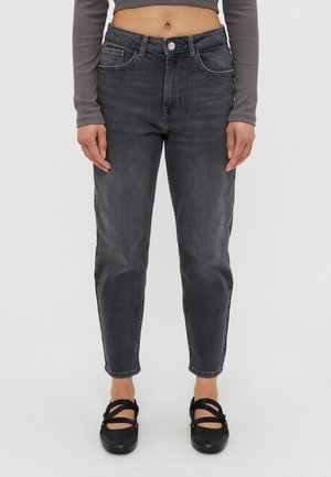 Person wearing high-waisted dark gray jeans, cropped gray long-sleeve top, and black Mary Jane shoes standing against white background.