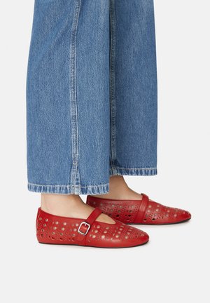 Zapatos planos rojos con detalles recortados, una correa con hebilla, combinados con pantalones anchos de mezclilla azul con borde dobladillado.