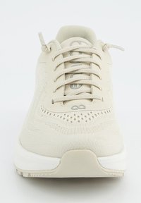 Beige Sport Schuh mit strukturiertem Mesh-Obermaterial, runder Zehenpartie und sechs Ösen für die Schnürsenkel; verfügt über eine kontrastierende weiße Sohle und kleine Belüftungslöcher.