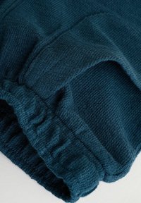 Dark teal textured fabric with elasticated cuff detail, likely a sleeve or pant leg, shown in close-up on a light background.