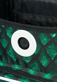 Zelená a černá vzorovaná látka s diamantovým designem a bílým kruhovým zámkem. Texturovaný povrch a černé detaily zipu.