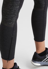 Leggings sportivi neri e texture con una tasca con zip lungo la parte bassa della gamba e una vestibilità affusolata, abbinati a sneaker scure.