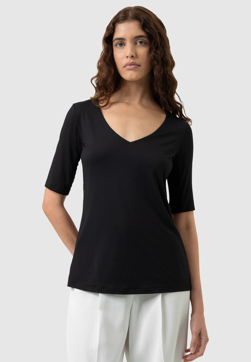 Black V-neck t-shirt with short sleeves, made of soft fabric. Features a relaxed fit and smooth texture, worn with white trousers.