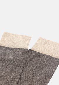 Šedé a béžové pletené ponožky s texturovanou tkaninou. Kontrastní žebrované lemy v béžové barvě na vrchu a hladké šedé tělo, které sahá dolů.