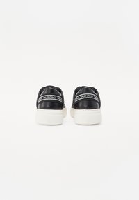 Des baskets en cuir noir avec des semelles en caoutchouc blanc, présentant une texture matelassée et une marque bien visible au dos.