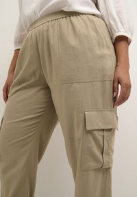 Beige cargobyxor med elastisk midja, sidofickor och texturerad tyg. Har en avslappnad passform och fickor i lappen på låren.