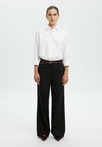 Witte blouse met opgerolde mouwen, gecombineerd met ruime zwarte broek en een bordeauxrode riem, afgemaakt met pointed zwarte schoenen.