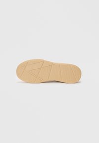 Gummisål i beige med en teksturert overflate og trekantet mønster. Har definerte spor for bedre grep og trekkraft.