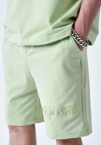 Shorts vert clair avec une texture douce, affichant un logo brodé "Project x Paris" et des poches latérales. Associés avec un haut assorti.