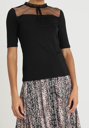 Mujer con una blusa negra con canesú de malla y mangas cortas, combinada con una falda plisada con un estampado de piel de serpiente.