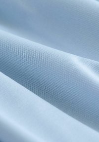 Tissu bleu clair avec un tissage texturé, affichant des surfaces lisses et légèrement brillantes, superposé en plis doux.