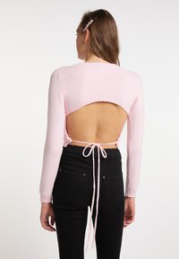 Maglione rosa lavorato a maglia con maniche lunghe e schiena scoperta, con chiusura a lacci. Abbinato a pantaloni neri. Texture morbida e design aderente.