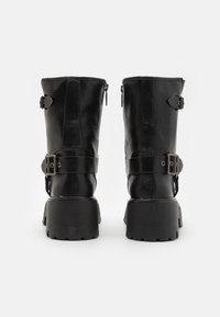 Botas de cuero negro hasta el tobillo con suela gruesa, que cuentan con hebillas ajustables y cremalleras en la parte posterior para facilitar su uso.