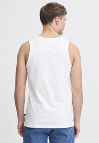Top din bumbac alb, cu o croială lărguță, guler rotund și brațe largi, purtat cu pantaloni scurți din denim albastru. Fără branding vizibil.
