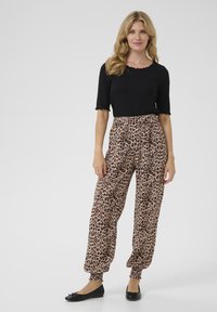 Top nero a costine con scollatura a pizzo abbinato a pantaloni leopardati a vita alta e dalla vestibilità ampia, con polsini elasticizzati. Ballerine nere.