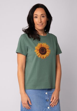 Grünes Baumwoll-T-Shirt mit einem großen Sonnenblumenmotiv in Gelb und Braun in der Mitte. Kurze Ärmel, Rundhalsausschnitt.