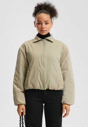 Veste courte beige clair avec une fermeture éclair à l'avant, un col pointu et une taille élastique. Tissu lisse et mat avec une coupe décontractée et des manches longues.