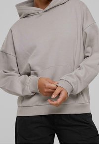 Sweat à capuche gris clair en tissu doux, avec une poche frontale, une coupe oversize et des poignets et un ourlet côtelés. Assorti à un pantalon noir.