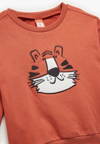Sweter w kolorze rdzawej pomarańczy z haftem w kształcie twarzy tygrysa w czerni i bieli, z okrągłym dekoltem i miękką teksturą.