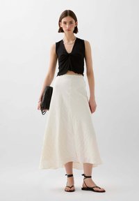 Schwarzes, kurzes Top mit Raffung, weiße, strukturierte Maxiröcke, schwarze Handtasche und schwarze Sandalen mit Riemen. Schlichte, moderne Silhouette und Farbkontrast.